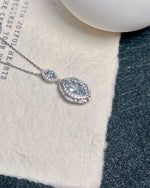 On-hand shot of Marquise cut aquamarine halo necklace featuring Marquise Cut center stone